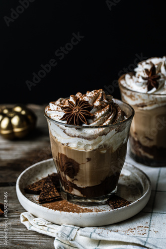 Two glasses of Pumpkin pie spice mocha latte with whipped cream and dark chocolate on plate on wooden table on dark background .