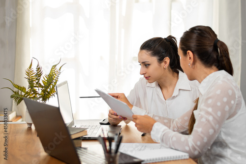 Mujeres de negocios observan datos en su laptop y conversan mientras trabajan en la oficina. photo