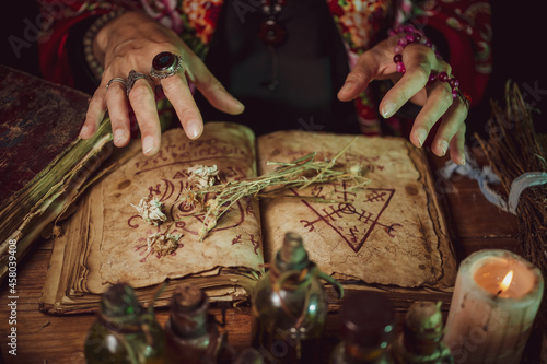Obraz na plátně Female witch making potion on dark background, magic bottles with potions and ca