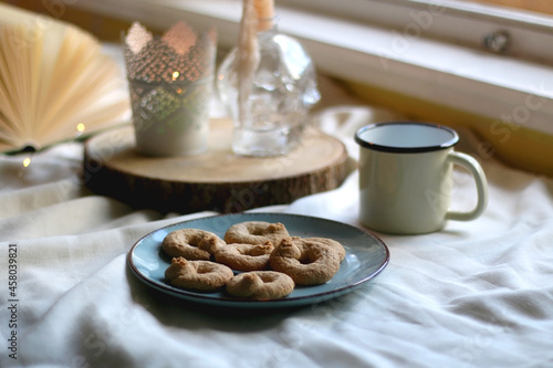 Plate with cookies, open book, lit candles and fairy lights. Hygge at home. Selective focus.