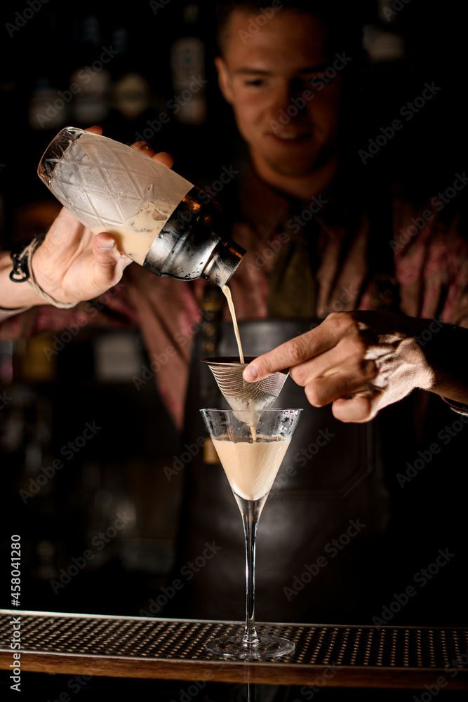 martini glass and male hand holding sieve over it and pour liquid from shaker