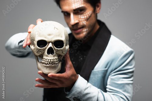 blurred man in halloween makeup showing scary skull while looking at camera isolated on grey © LIGHTFIELD STUDIOS