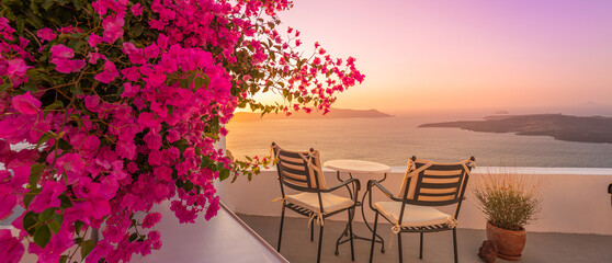 Summer sunset vacation scenic of luxury famous Europe destination. White architecture in Santorini, Greece. Stunning travel scenery with pink flowers chairs, terrace sunny blue sky. Romantic street