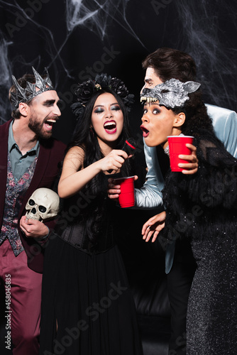 interracial women in halloween costumes singing karaoke near friends on black