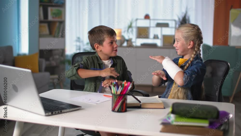 online education, children communicate while sitting at a table with laptop during an online lesson, girl with a plaster cast gestures in front of the boy online education, children communicate while sitting at a table with laptop during an online lesson, girl with a plaster cast gestures in front of the boy