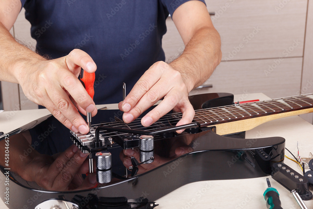 Guitar master adjusts tremolo bridge on modern electric guitar. Photos |  Adobe Stock