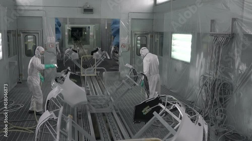 Painting vehicle parts in sprcial booth. Car manufacturing factory. Two painters spray white paint on a bumper car.