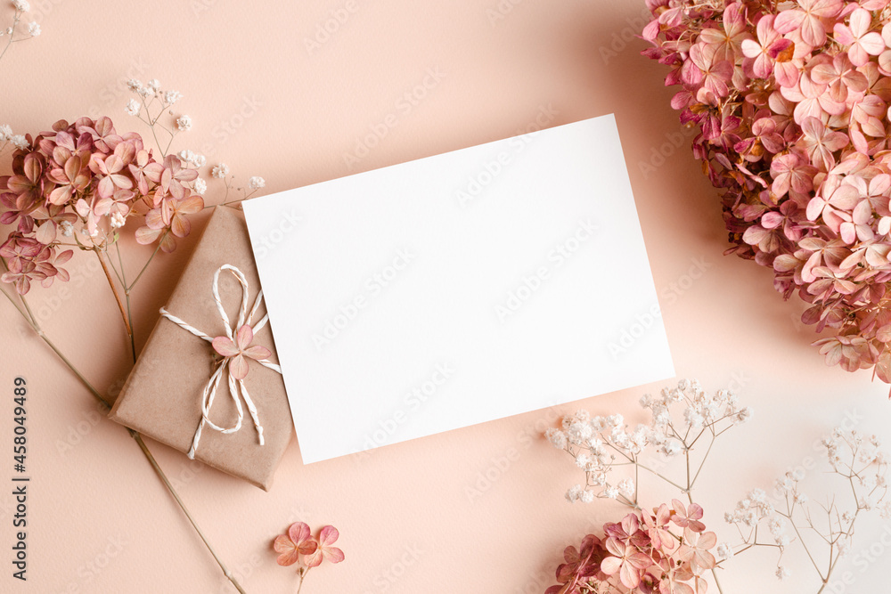 Invitation or greeting card mockup with gift box, hydrangea and gypsophila flowers decorations. Empty card mockup on pink background.