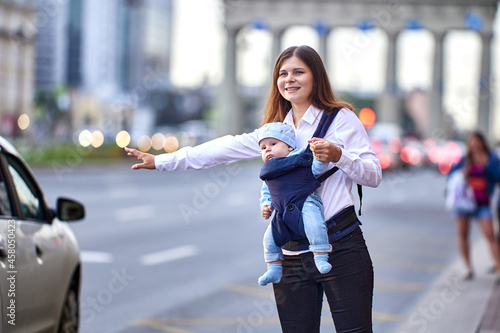 Woman with child in baby sling stops taxi on busy city street. photo