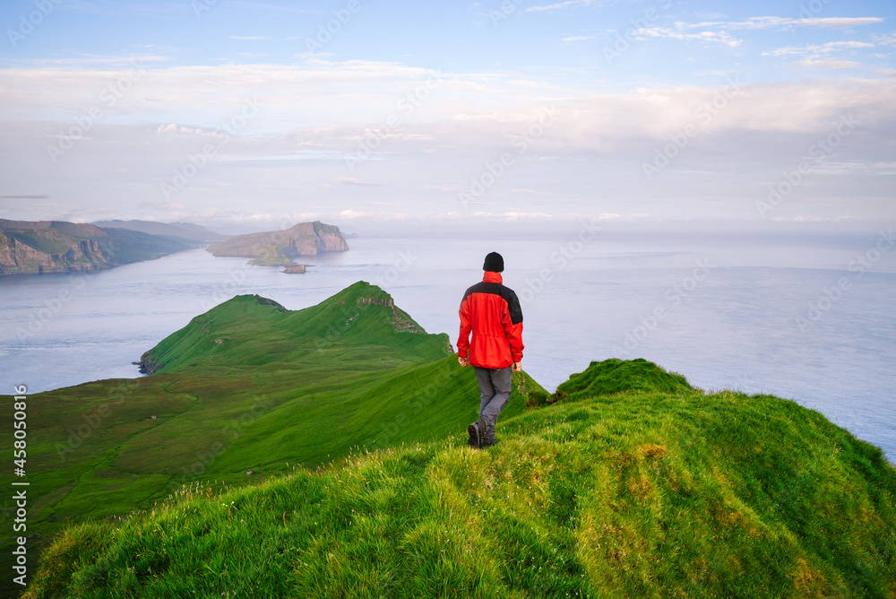 Fototapeta premium A tourist walks through the green hills on Mykines island, Faroe Islands