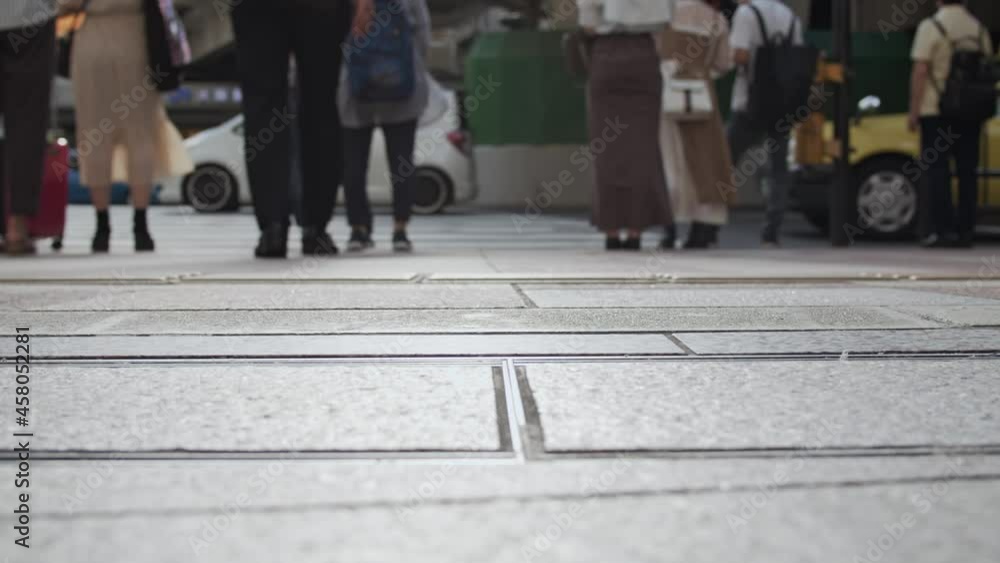赤信号の横断歩道に並び、信号を待つ人々の足元。 赤信号の横断歩道に並び、信号を待つ人々の足元。