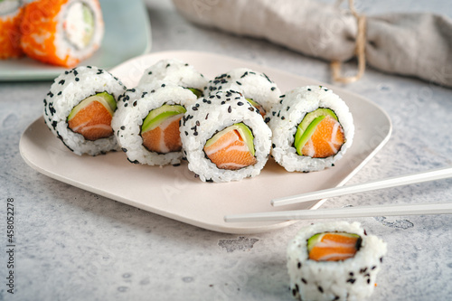 A set of fresh sushi rolls with salmon, avocado and black sesame seeds served on a plate with chopsticks.  California roll
