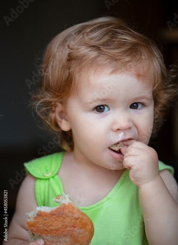 Portrait of cute baby with bread in her hands eating. Cute toddler child eating sandwich  self feeding concept.