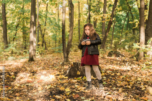 A little girl take a photo with old retro camera in autumn nature. Leisure and hobby concept.