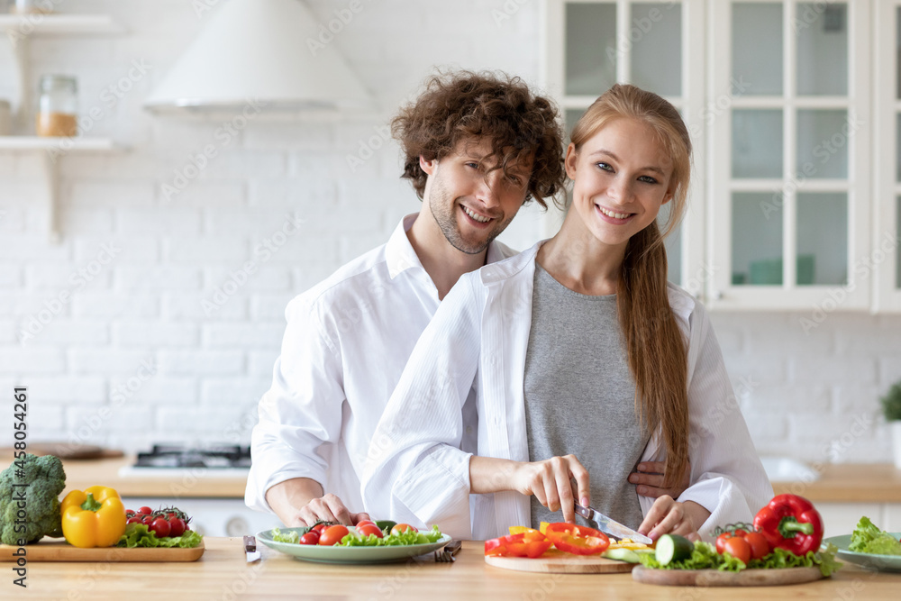 Lovely young couple cooking salad together in kitchen. Healthy food.