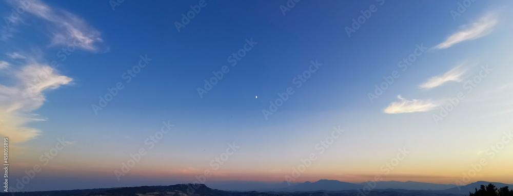 Tramonto estivo sui monti Appennini con la Luna nel cielo azzurro limpido