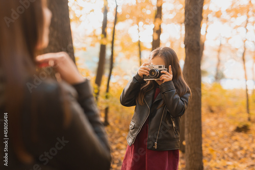 Child girl photographer takes pictures of a mother in the park in autumn. Hobbies, photo art and leisure concept.