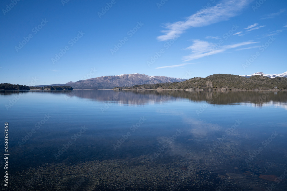 The lake in a sunny morning. Panorama view of the forest, lake and the perfect reflection of the sky in the blue water. The Andes mountain range in the background.