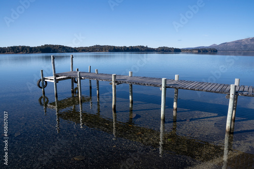 The wooden docks in the calm lake. The clear blue sky and pier reflected in the water surface. The forest and mountains in the background. photo