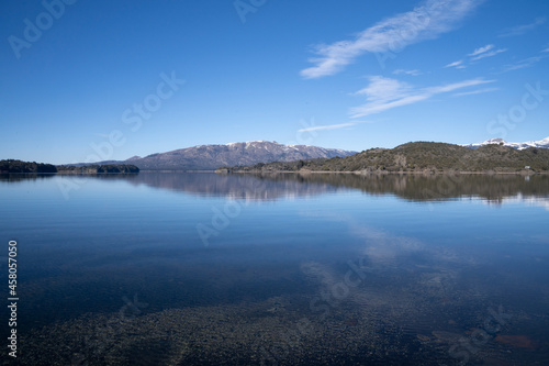 The lake in a sunny morning. Panorama view of the forest, lake and the perfect reflection of the sky in the blue water. The Andes mountain range in the background.