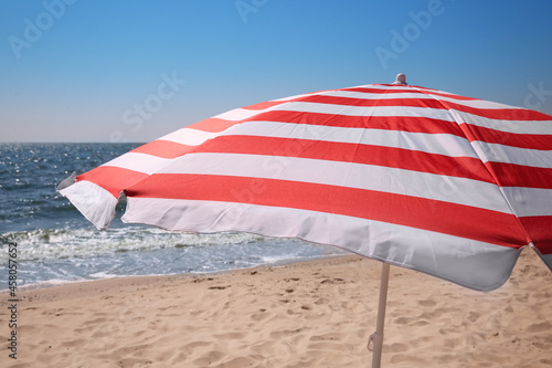 Red and white striped beach umbrella on sandy seashore