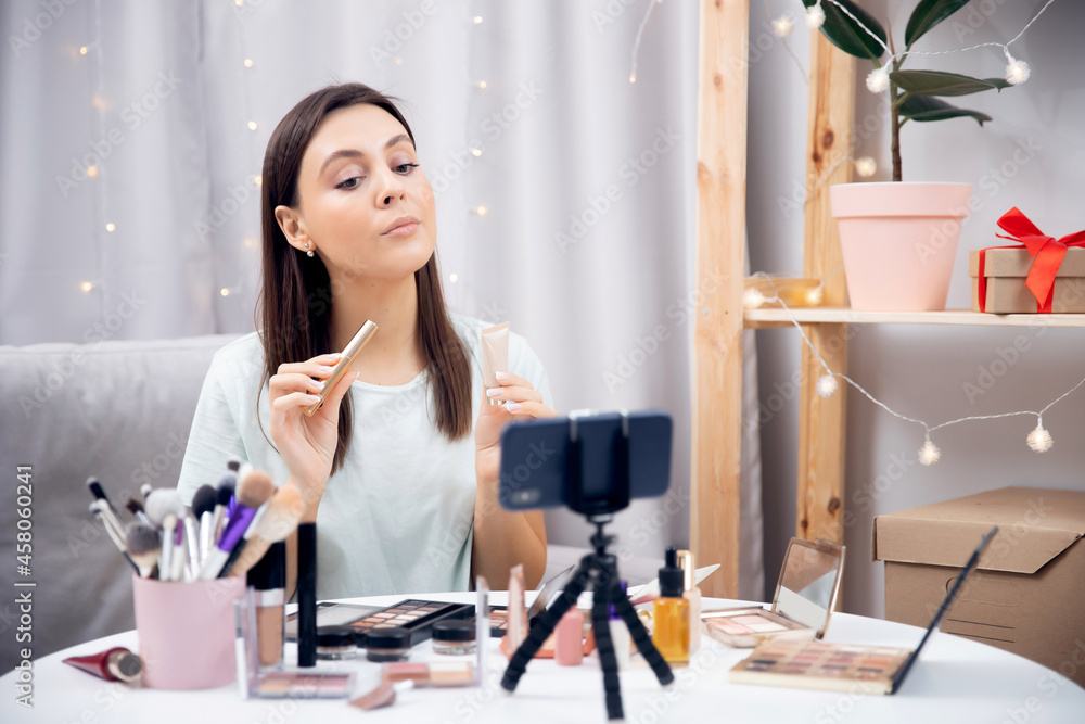 Happy woman vlogger is showing cosmetics products while recording video stream on phone. Concept Influencer blogger beauty blog Happy woman vlogger is showing cosmetics products while recording video stream on phone. Concept Influencer blogger beauty blog