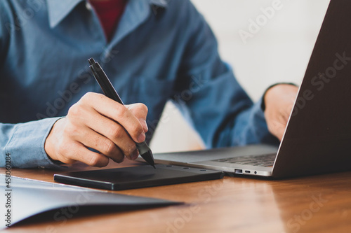 Businessman working on laptop holding stylus writing on touchpad.