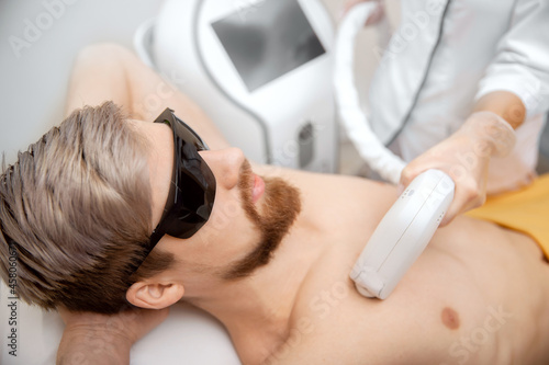 Woman worker beauty salon giving man torso hair removal laser epilation studio