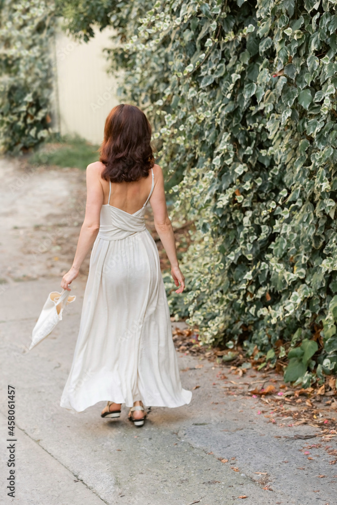 Back view of a girl with reusable bag in a natural dress against the background of a green wall of leaves in the street.  Eco-friendly product concept.