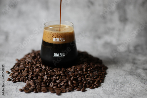 Spray of dark beer with foam in glass with low and high fuel on coffee beans with grey background. photo