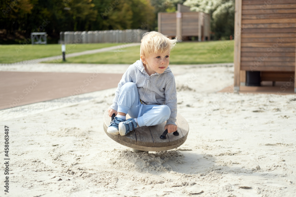 Little caucasian blond boy playing on kids playground in a sunny autumn day Little caucasian blond boy playing on kids playground in a sunny autumn day