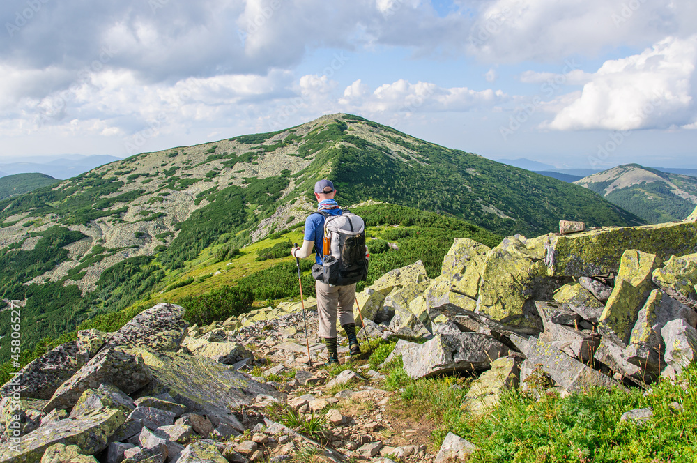 A tourist with a large backpack climbs a mountain stone path high in the Carpathian 
