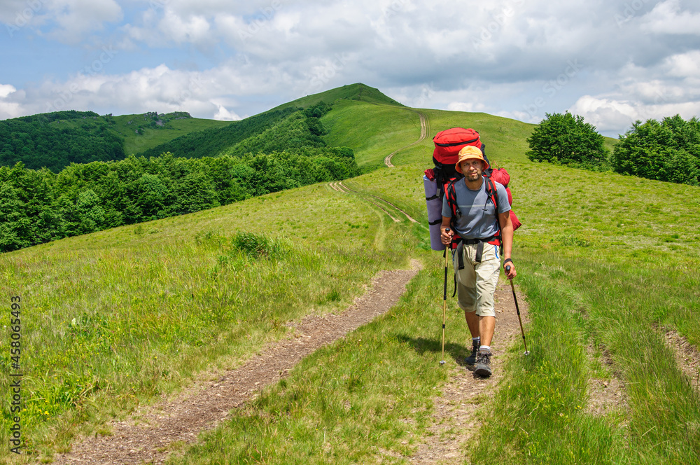 Obraz premium A male tourist with a large backpack climbs a mountain stone path high in the Carpathian 