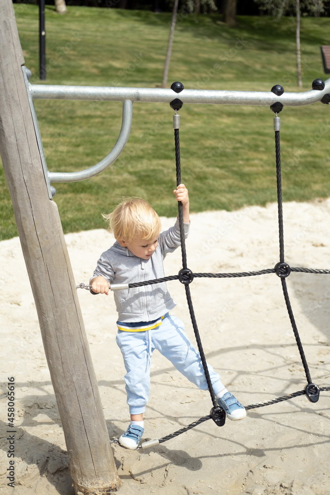 Little caucasian blond boy playing on kids playground in a sunny autumn day Little caucasian blond boy playing on kids playground in a sunny autumn day