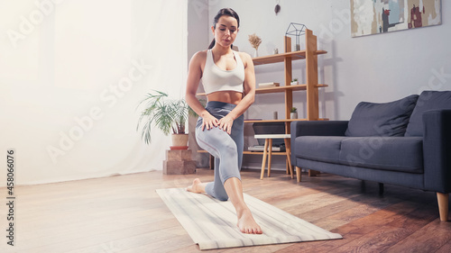 Barefoot sportswoman stretching leg on striped fitness mat at home