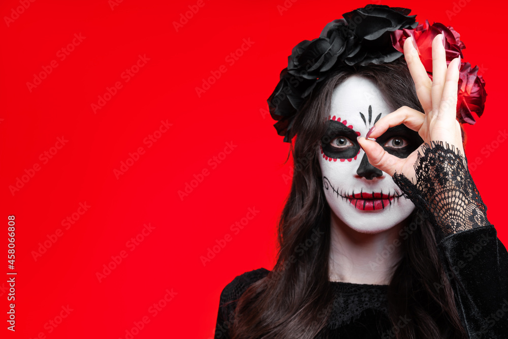 Girl with creative sugar skull makeup with a wreath of flowers on head, wide isolated on red background. Holiday concept Dia De Los Muertos on poster for Halloween party or La Calavera Catrina. Girl with creative sugar skull makeup with a wreath of flowers on head, wide isolated on red background. Holiday concept Dia De Los Muertos on poster for Halloween party or La Calavera Catrina.