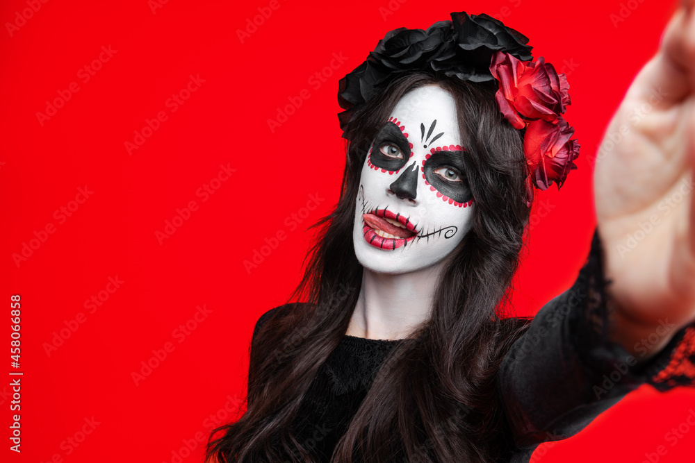 Girl with creative sugar skull makeup with a wreath of flowers on head, wide isolated on red background. Holiday concept Dia De Los Muertos on poster for Halloween party or La Calavera Catrina. Girl with creative sugar skull makeup with a wreath of flowers on head, wide isolated on red background. Holiday concept Dia De Los Muertos on poster for Halloween party or La Calavera Catrina.