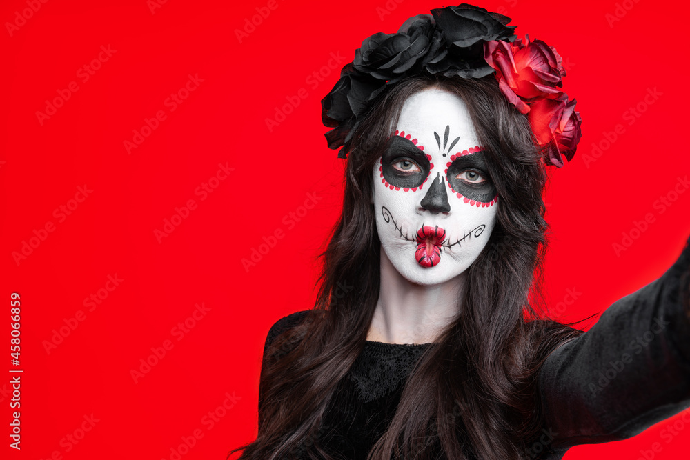 Girl with creative sugar skull makeup with a wreath of flowers on head, wide isolated on red background. Holiday concept Dia De Los Muertos on poster for Halloween party or La Calavera Catrina. Girl with creative sugar skull makeup with a wreath of flowers on head, wide isolated on red background. Holiday concept Dia De Los Muertos on poster for Halloween party or La Calavera Catrina.