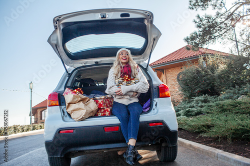 The girl is smiling and sit in the trunk of the car with x-mas boxes. the New Year's mood. Beautiful woman dressed sweater and jeans preparing for Christmas or New year's eve celebrations, buys gifts 