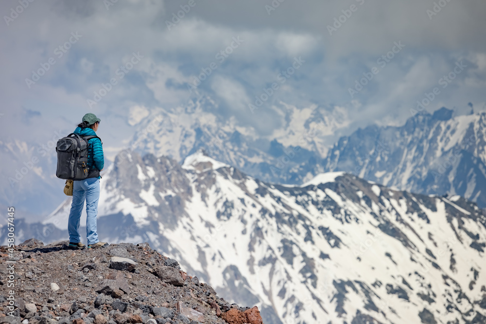 Hiker woman standing up achieving the top. View at the snowy mountains.