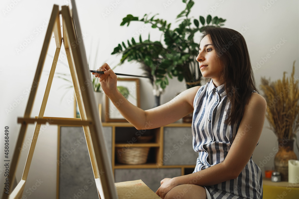 A young woman artist paints in her apartment with oil paints. Female student draws in art studio.Fine art study concept. A young woman artist paints in her apartment with oil paints. Female student draws in art studio.Fine art study concept.