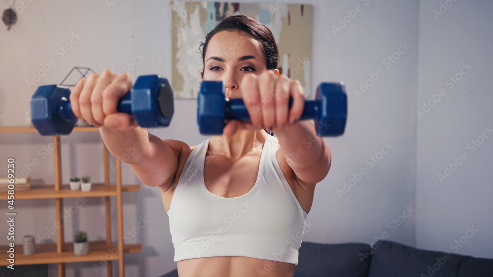 Sportswoman training with blurred dumbbells at home Sportswoman training with blurred dumbbells at home