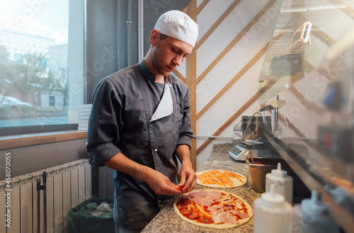 The cook puts the ingredients on the pizza dough. Catering kitchen work.