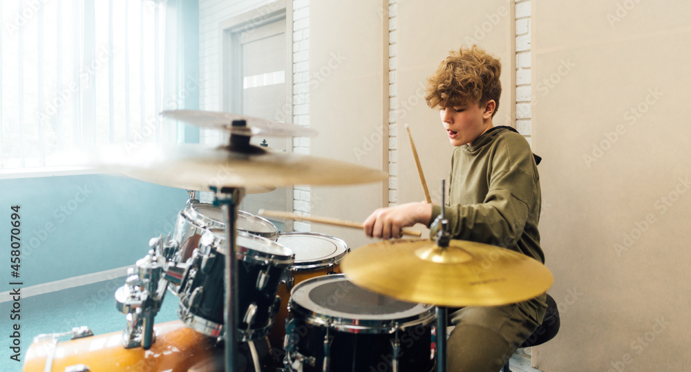 Obraz premium Young teen boy plays drums vigorously in the studio.