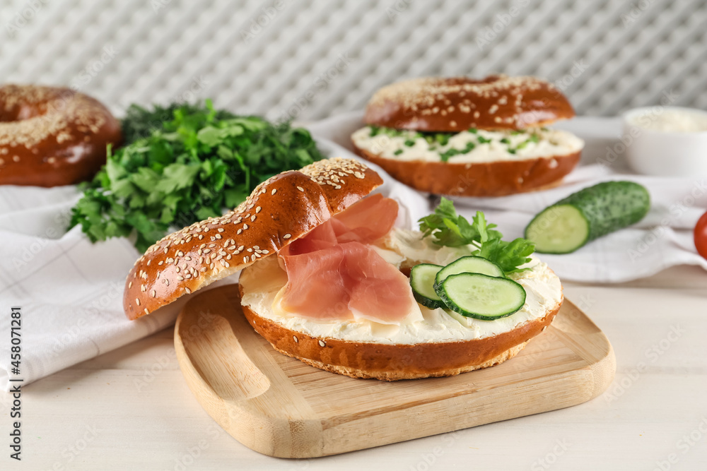 Delicious bagel with cream cheese, jamon, cucumber and parsley on white wooden table Delicious bagel with cream cheese, jamon, cucumber and parsley on white wooden table
