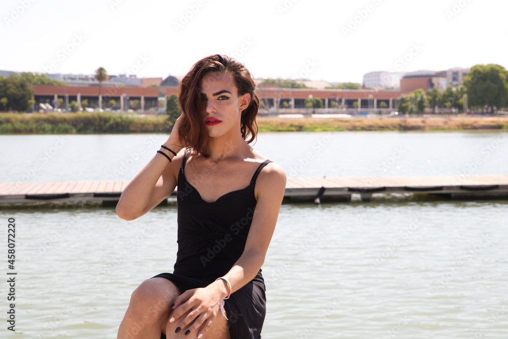 young latina and transsexual woman sitting on the river pier in a black dress. Concept diversity, transgender, and freedom of homosexual expression.