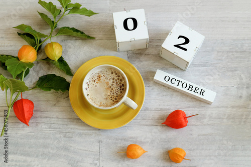 Calendar for October 2 : the name of the month in English, cubes with the numbers 0 and 1, a yellow cup with hot coffee, branches of physalis with orange boxes on a gray background photo