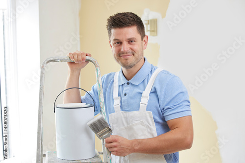 Portrait Of Man Wearing Overalls Painting Wall In Room Of House With Brush photo