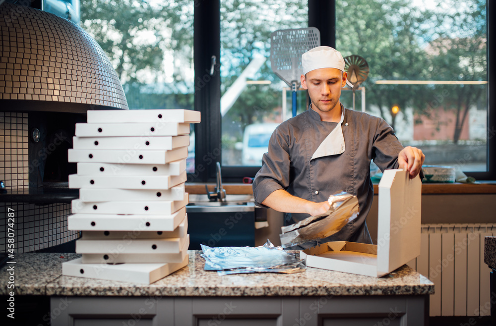 Pizzeria worker folds foil into pizza box. Catering kitchen work. - obrazy, fototapety, plakaty 