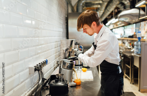 Fototapeta Naklejka Na Ścianę i Meble -  The waiter makes orange juice with a juicer. Catering kitchen work.